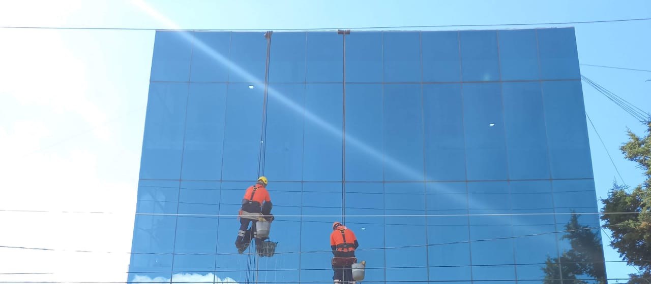 Técnicos de Empresa Limpia en rappel limpiando la fachada de vidrio de un edificio